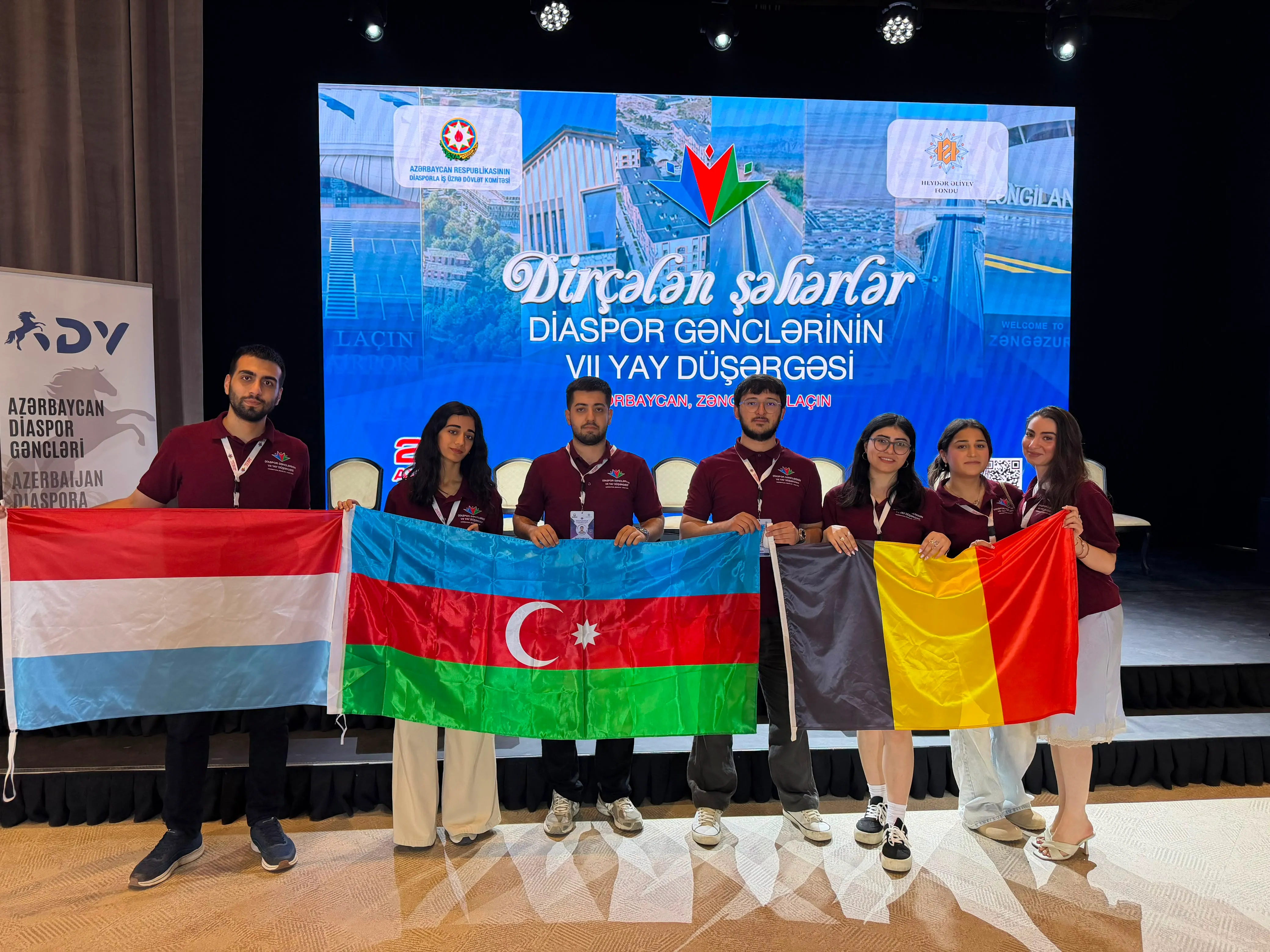 Des participants au camp tiennent les drapeaux du Luxembourg, de l'Azerbaïdjan et de la Belgique devant la scène